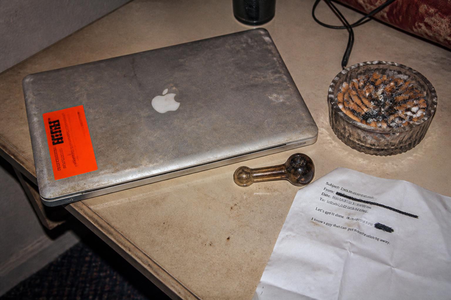 closed macbook w/ $CRACKTOP sticker, pipe, ashtray, printed email